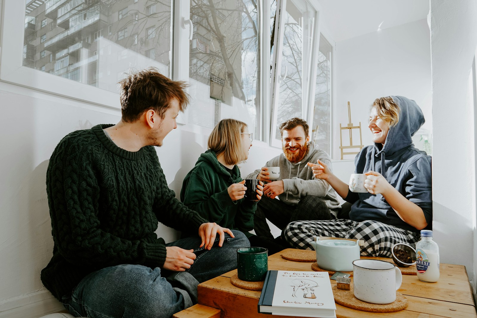 Four people around a table with mugs, mid-conversation